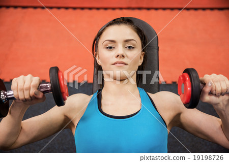 Focused woman lifting dumbbells while lying down Focused woman lifting dumbbells while lying down 19198726