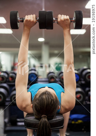Woman lifting dumbbell weights while lying down Woman lifting dumbbell weights while lying down 19198975