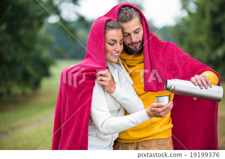 Happy couple under a blanket pouring hot drink Happy couple under a blanket pouring hot drink 19199376