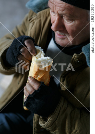 Depressed senior-aged beggar eating bread.  19253399