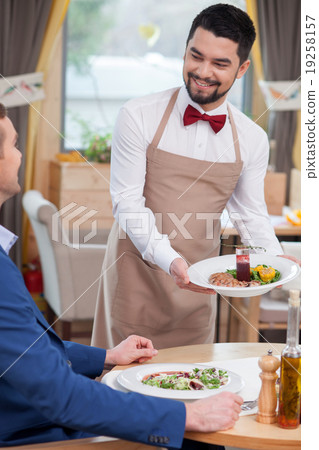 Cheerful male cafe worker is serving a customer Cheerful male cafe worker is serving a customer 19258157