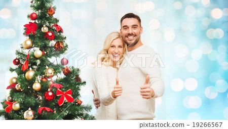 happy couple showing thumbs up with christmas tree happy couple showing thumbs up with christmas tree 19266567
