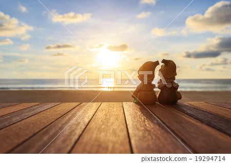 Two dolls sitting on wooden table at sunset beach Two dolls sitting on wooden table at sunset beach 19294714