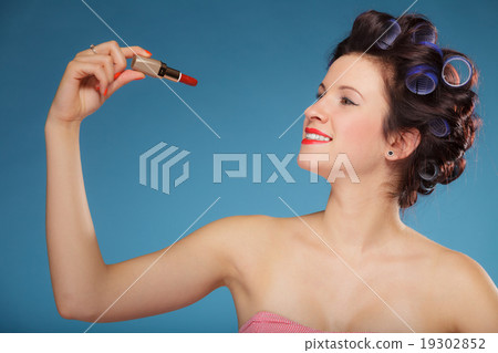 Girl in hair curlers applying red lipstick 19302852