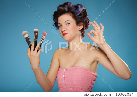 woman in hair rollers holds makeup brushes 19302854