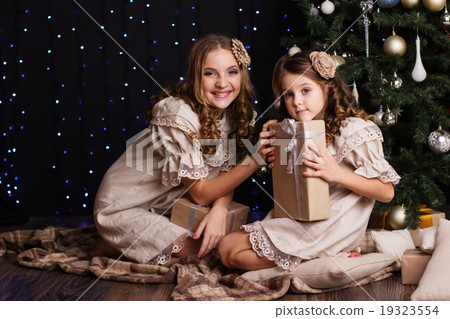 Two girls are sharing gifts near christmas tree Two girls are sharing gifts near christmas tree 19323554