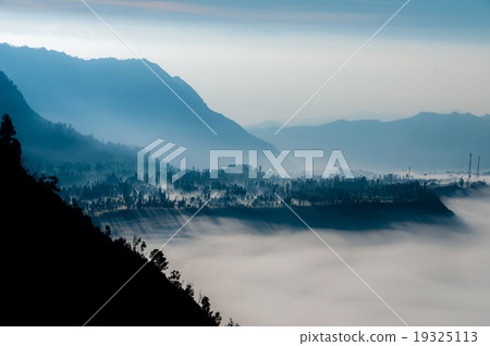 Steep black mountain silhouette in front of thick Steep black mountain silhouette in front of thick 19325113