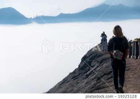 Woman walking along top of volcano next to fog and Woman walking along top of volcano next to fog and 19325128
