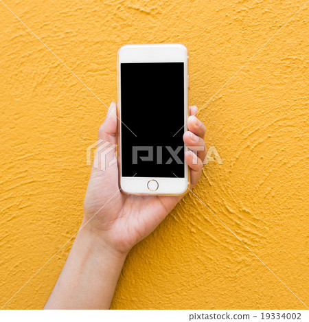 Hand holding white Smartphone on yellow wall  19334002
