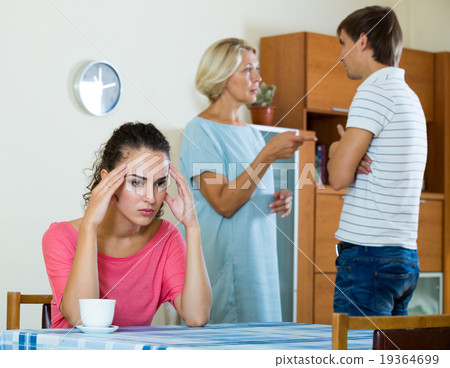 Sad young woman watching husband and mother having fight Sad young woman watching husband and mother having fight 19364699