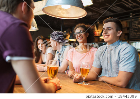 happy friends drinking beer and talking at bar 19443399