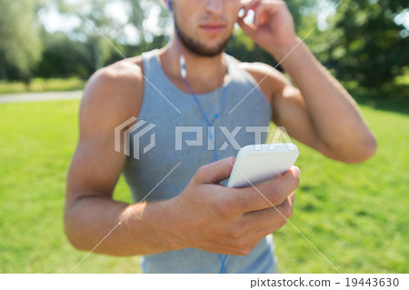 young man with earphones and smartphone at park young man with earphones and smartphone at park 19443630