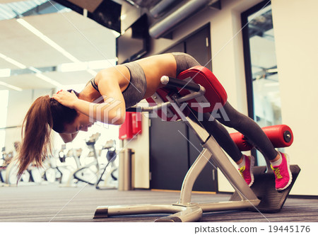 young woman flexing back muscles on bench in gym 19445176