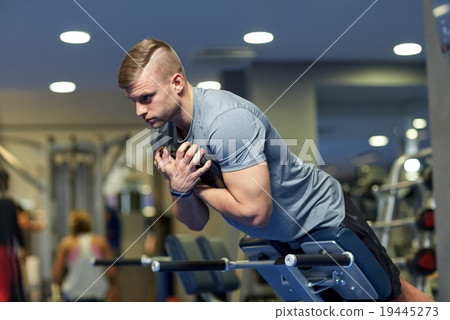 young man flexing back muscles on bench in gym 19445273