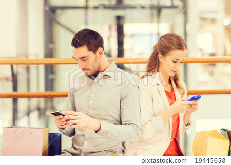couple with smartphones and shopping bags in mall 19445658