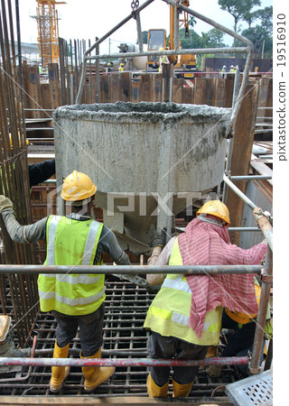 Workers pouring concrete into pile cap formwork 19516910