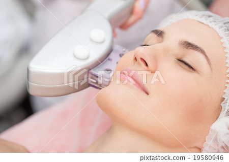 Skillful young cosmetologist is treating female 19580946