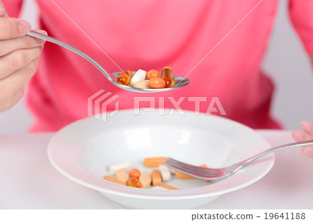Young women eating medicine capsules on spoon Young women eating medicine capsules on spoon 19641188