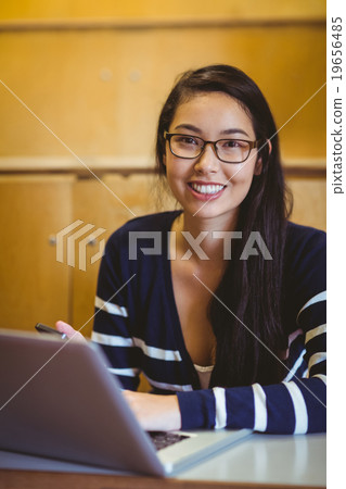 Smiling student using laptop during class 19656485