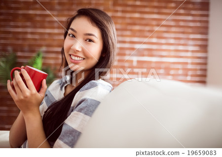 Smiling asian woman on couch having hot drink 19659083