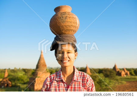 Young Asian traditional female farmer carrying clay pot on head Young Asian traditional female farmer carrying clay pot on head 19680561