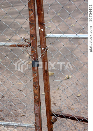 a metallic padlock and chain lock at fence door. a metallic padlock and chain lock at fence door. 19704491
