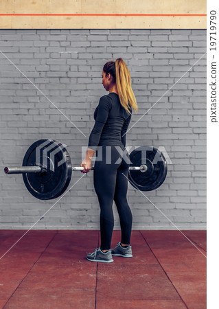 Full length young woman lifting barbell in gym Full length young woman lifting barbell in gym 19719790