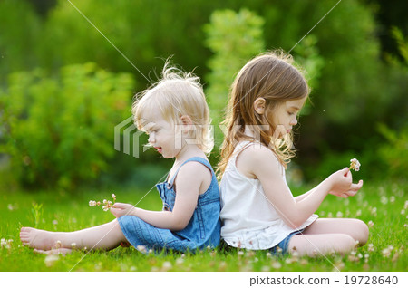 Two sisters sitting on the grass on summer day Two sisters sitting on the grass on summer day 19728640