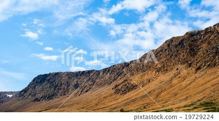 Rocky dry yellow cliff slope against blue sky Rocky dry yellow cliff slope against blue sky 19729224