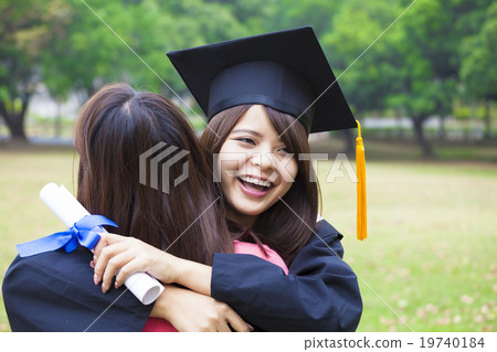 young female graduate hugging her friend at graduation ceremony 19740184