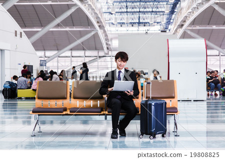 在機場大廳檢查個人計算機的商人 在機場大廳檢查個人計算機的商人 19808825