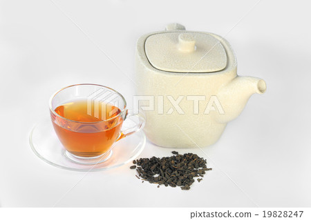 White teapot, a cup of tea and dried tea leaves. 19828247
