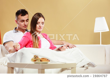 Couple reading ebook relaxing at home on sofa. Couple reading ebook relaxing at home on sofa. 19864787