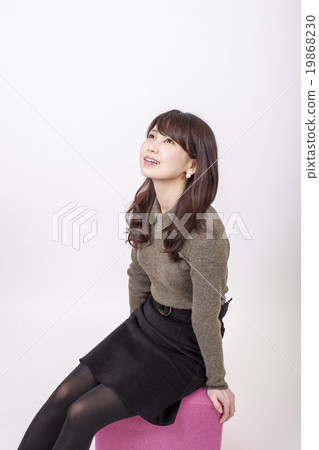 一個少婦坐在白色背景前面的一把桃紅色椅子和觀看 一個少婦坐在白色背景前面的一把桃紅色椅子和觀看 19868230