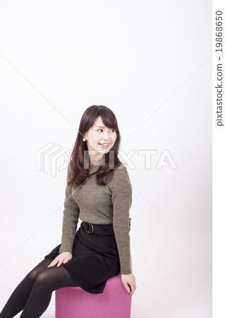 Smiling young woman sitting in a pink chair in front of a white background and turning backwards 19868650