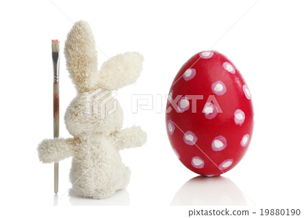 Stuffed Easter bunny paints a red Easter egg Stuffed Easter bunny paints a red Easter egg 19880190