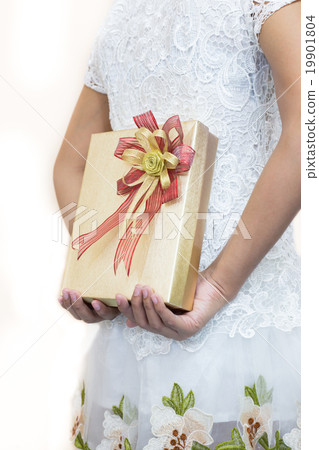 Women in white hiding a gift behind her back. Women in white hiding a gift behind her back. 19901804