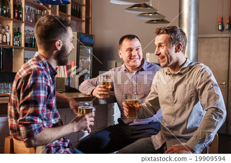 Happy friends drinking beer at counter in pub Happy friends drinking beer at counter in pub 19909594