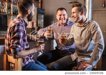 Happy friends drinking beer at counter in pub Happy friends drinking beer at counter in pub 19909596
