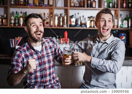 Young people with beer watching football in a bar Young people with beer watching football in a bar 19909598