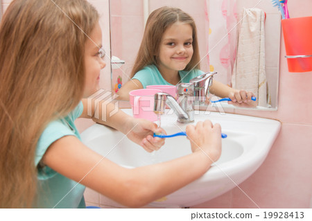 The girl washes a toothbrush under the tap 19928413