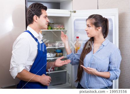 Serviceman asking housewife of technical problems with fridge Serviceman asking housewife of technical problems with fridge 19953556
