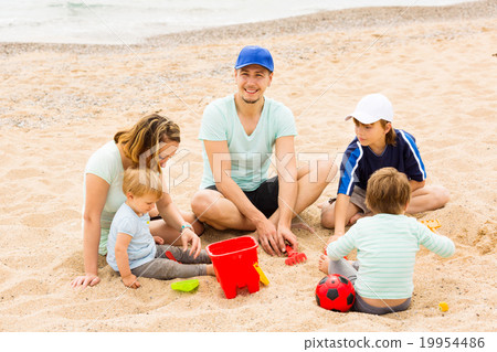 Positive family of five sitting at sandy beach 19954486