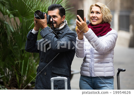 couple walking with luggage, camera and smartphone couple walking with luggage, camera and smartphone 19954626