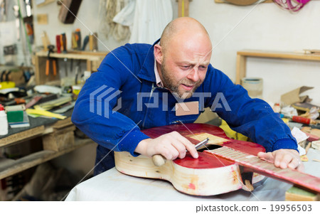 craftsman working with unfinished guitar 19956503