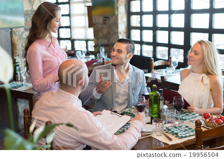 Waiter with restaurant guests at table 19956504