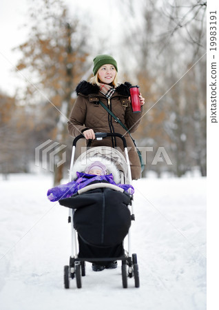 Young mother walking with baby in stroller in winter Young mother walking with baby in stroller in winter 19983191