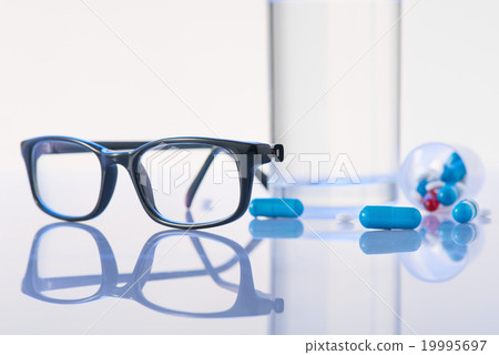 Glasses, pills and water glass are on the surface. Glasses, pills and water glass are on the surface. 19995697