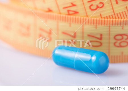 Blue pill and measuring tape on the surface. Blue pill and measuring tape on the surface. 19995744