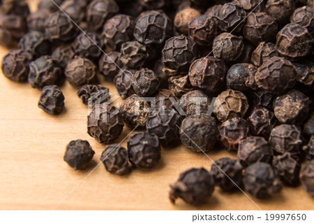 Heaps of black pepper corns on wooden surface Heaps of black pepper corns on wooden surface 19997650